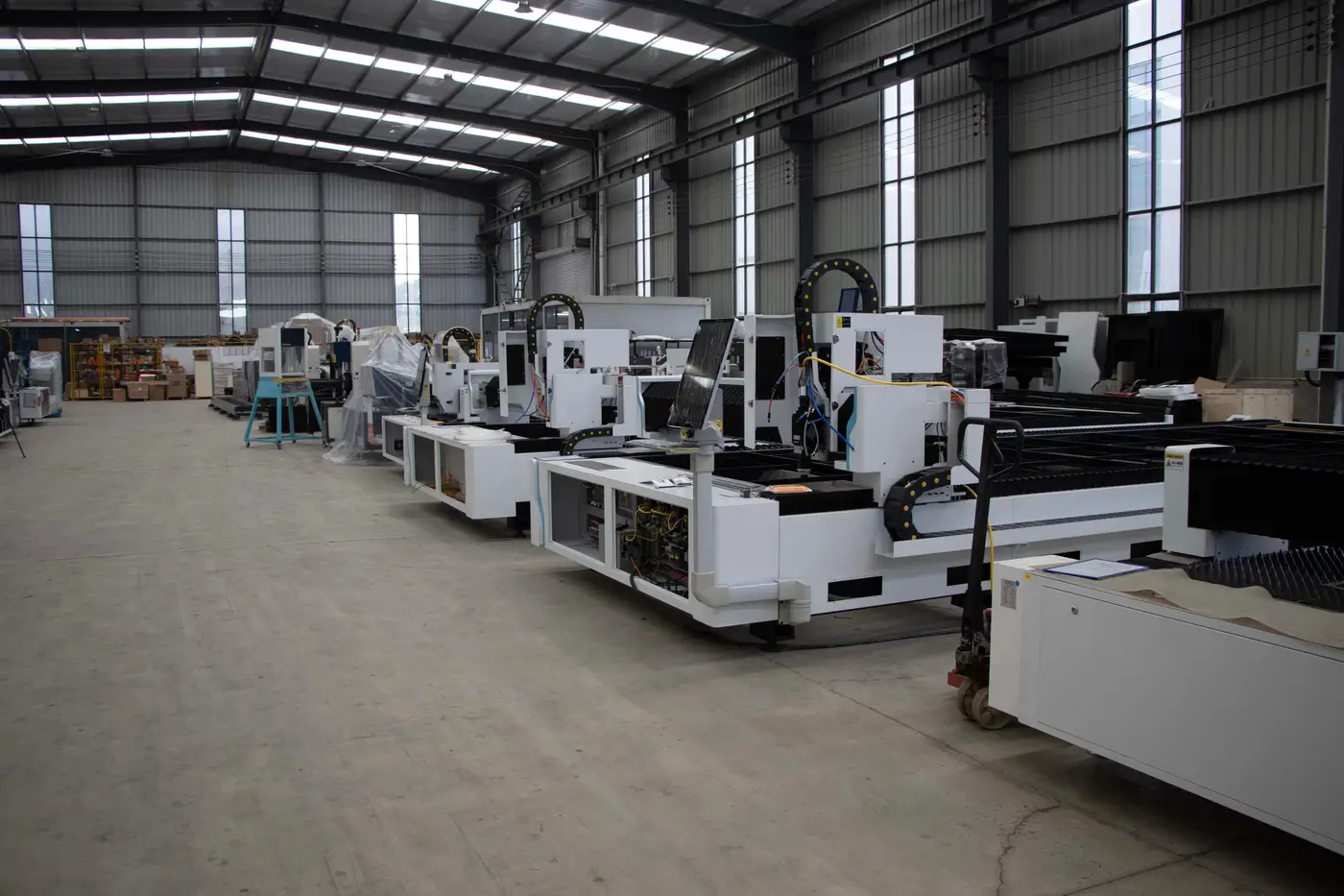 Row of industrial manufacturing machines lined up on the floor of a large metal-sided plant building.