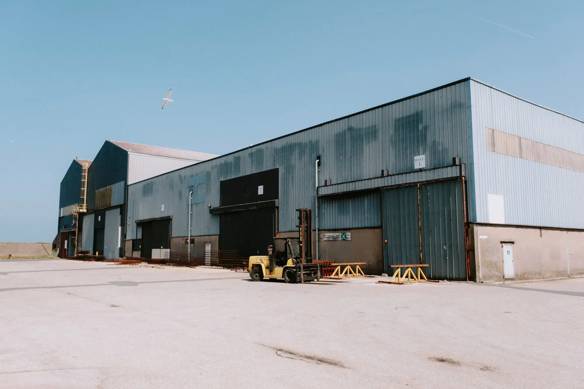 Steel-clad industrial sheds with an open concrete apron and a forklift in the yard